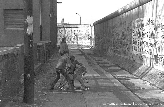 Mauerfoto: Spielende Kinder und Spaziererin entlang der Mauer