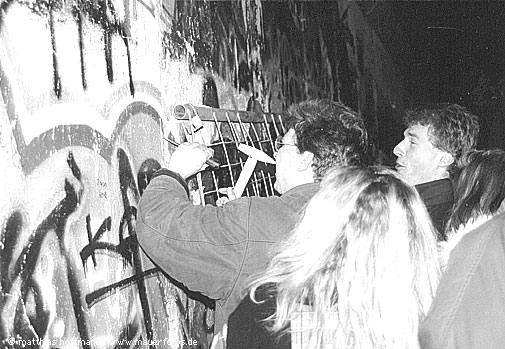 Mauerfoto: Eine Gruppe Menschen hÃ¤mmert StÃ¼cke aus der Mauer an der Bernauer StraÃŸe.